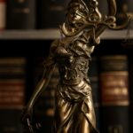 Close-up of a golden Lady Justice statue with scales in a law library setting.